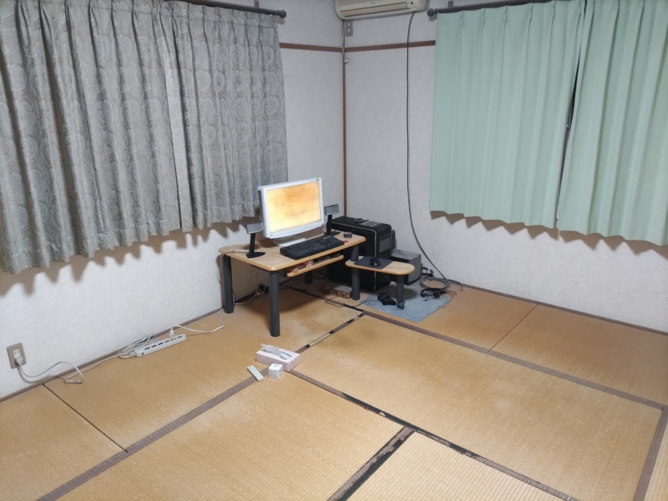 畳の部屋の一角に置かれたパソコンデスクと作業環境。引きこもり生活でほぼ24時間過ごしているシンプルな部屋の様子。